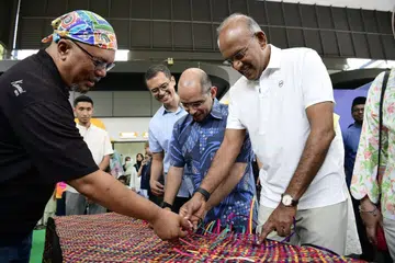 Menteri Kanan merangkap Menteri Penyelaras bagi Keselamatan Negara, Encik K. Shanmugam (kanan) dan Setiausaha Parlimen Kanan (Pendidikan merangkap Pembangunan Negara), Dr Syed Harun Alhabsyi (dua dari kanan) mencuba aktiviti menganyam dengan bimbingan pengasas Kamal Arts, Encik Kamal Dollah (kiri), semasa Raikan Ilmu@Heartlands (Nee Soon) di Yishun Town Square pada 5 September. Turut bersama dalam gambar ialah Pengerusi M³+@Nee Soon, Encik Ibrahim Ghouth Wu (tiga dari kanan).