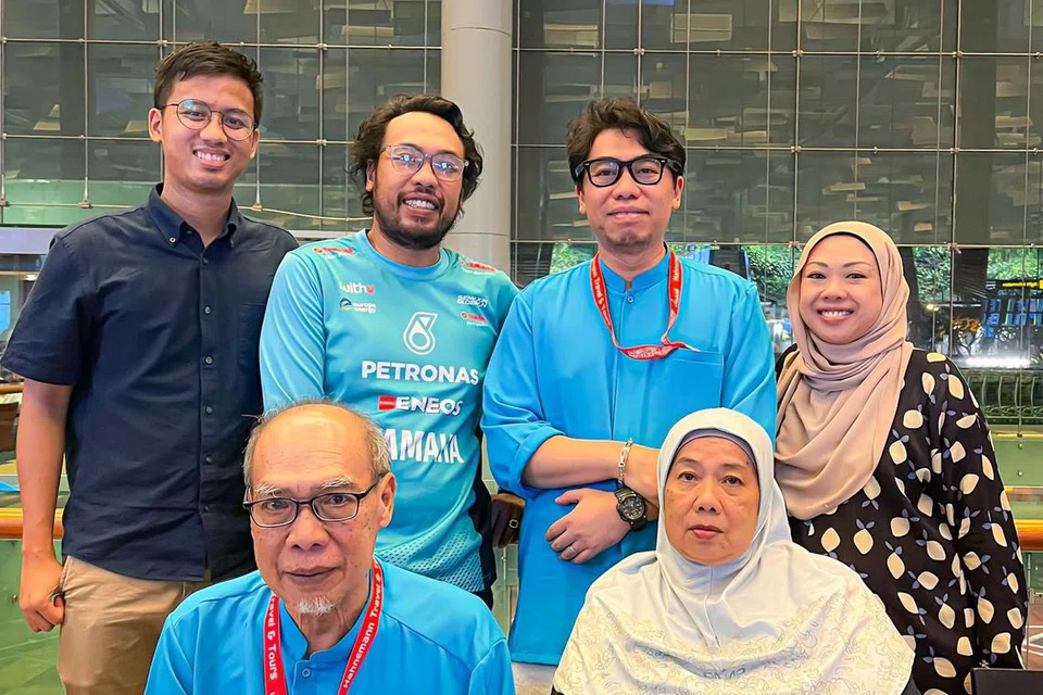 TETAP BERSEMANGAT: Encik Muhammad Suffian Apandi (berdiri dua dari kanan) dan Encik Apandi Radi (duduk) bersama keluarga mereka pada pagi Jumaat di Lapangan Terbang Changi.