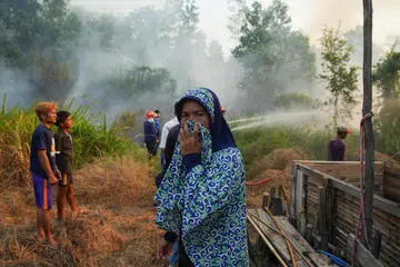 Seorang wanita menutup hidung ketika anggota bomba berusaha memadam kebakaran hutan dan tanah yang merebak berhampiran kawasan kediaman di Palembang, Sumatera Selatan, Indonesia, pada 10 Ogos 2026. Lebih 107,000 hektar kawasan di Indonesia terjejas akibat kebakaran tahun ini, dengan pemerintah meningkatkan operasi pemadaman dan pengubahsuaian cuaca ketika musim kemarau serta fenomena El Nino meningkatkan risiko kebakaran lebih meluas dan ancaman jerebu rentas sempadan