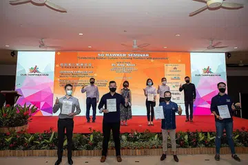 SAMPAIKAN ANUGERAH: Menteri Negara Kanan (Pengangkutan merangkap Kemampanan dan Sekitaran), Dr Amy Khor (di pentas, kedua dari kiri), di acara penyampaian Anugerah Penjaja Singapura kepada 15 penerima semalam semasa Seminar Penjaja SG di Our Tampines Hub. - Foto NEA