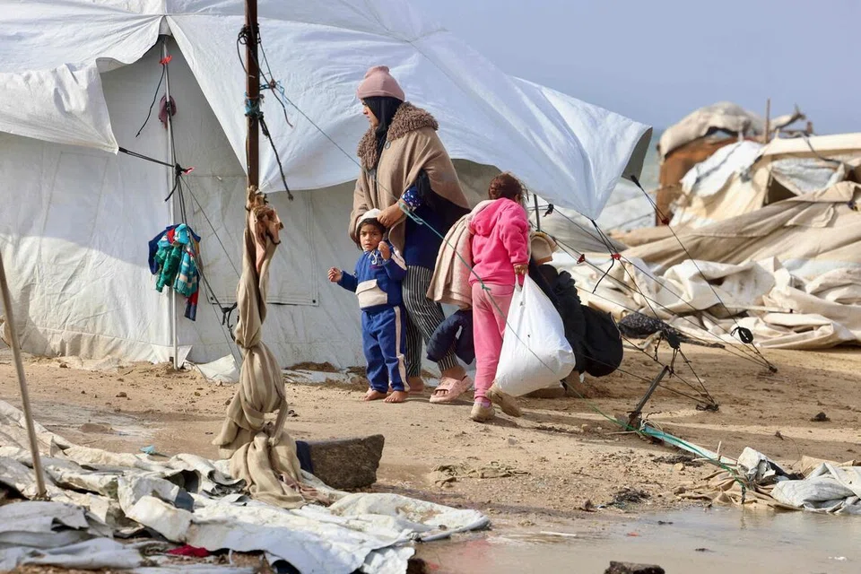 Seorang wanita Palestin yang dipindahkan memeluk seorang kanak-kanak berhampiran khemah dan tempat perlindungan sementara ketika wilayah itu dilanda cuaca musim sejuk di kem pelarian Al-Mawasi, selatan Jaluran Gaza, pada 29 Disember 2025. 