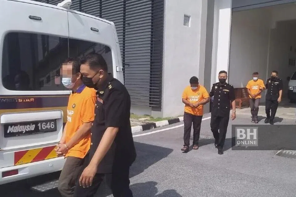 Suspek dibawa keluar dari mahkamah selepas direman bagi membantu siasatan terhadap dakwaan mengemukakan tuntutan palsu. 