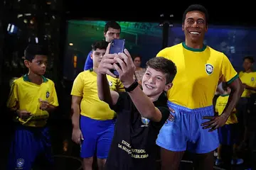 LEGENDA: Peminat bergambar bersama tugu Pele (kanan) di ibu pejabat Persekutuan Bola Sepak Brazil di Rio de Janeiro, Brazil. - Foto REUTERS