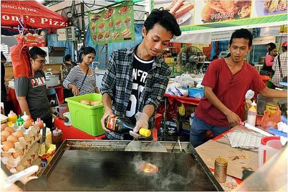 PERTAMA KALI BUAT BURGER RAMLY: Wartawan Berita Harian, Khairulameer Ramlan (kiri), memasak antara makanan terkenal di bazar Ramadan Geylang Serai, burger Ramly, bagi menimba pengalaman.