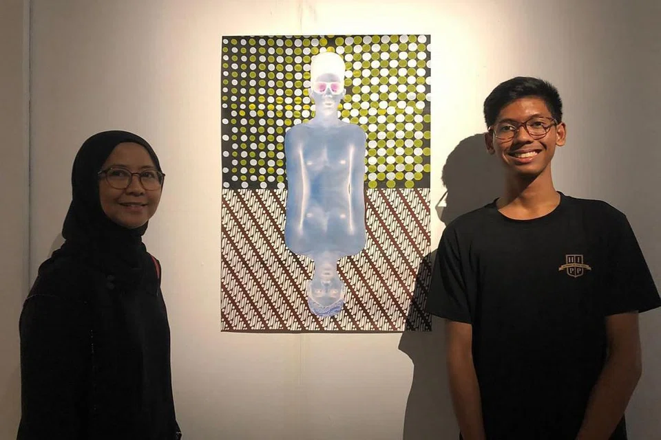 MAHU IKUT JEJAK ORANG TUA: Pelajar seni visual Sota, Izz Muhammad Ahmad bersama karya seninya bergambar dengan ibunya, Cik Norreha Sayuti. - Foto ihsan IZZ MUHAMMAD AHMAD