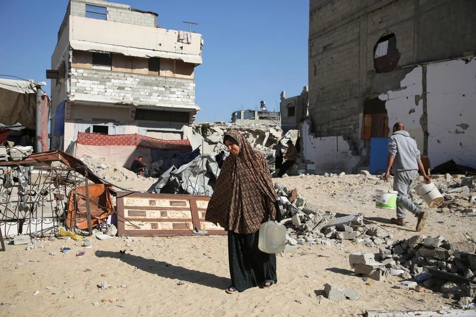 Wanita Palestin yang kehilangan tempat tinggal, Cik Makram Hamdouna, membawa bekas air di luar tempat perlindungannya di Khan Younis, selatan Gaza.