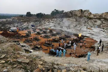 MEDAN BAKAR MAYAT: (Atas) Sukarelawan dan ahli keluarga buat persiapan bakar mayat mangsa Covid-19 di kampung Giddenahalli, luar kawasan Bengaluru, India. Seorang lelaki berpakaian alat pelindung diri (PPE) membakar sekujur mayat mangsa Covid-19 di pusat pembakaran mayat di Kathmandu, Nepal. - Foto-foto REUTERS
