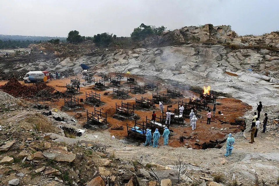 MEDAN BAKAR MAYAT: (Atas) Sukarelawan dan ahli keluarga buat persiapan bakar mayat mangsa Covid-19 di kampung Giddenahalli, luar kawasan Bengaluru, India. Seorang lelaki berpakaian alat pelindung diri (PPE) membakar sekujur mayat mangsa Covid-19 di pusat pembakaran mayat di Kathmandu, Nepal. - Foto-foto REUTERS