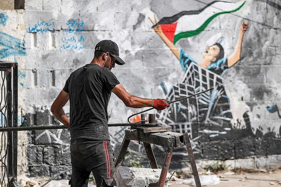 BANGKIT SEMULA: Seorang pekerja kelihatan meluruskan batang keluli sebagai sebahagian daripada usahanya mengitar semula barangan binaan dari bangunan yang musnah dan runtuh semasa peperangan antara Palestin dan Israel di Kota Gaza pada 5 Jun lalu. - Foto AFP