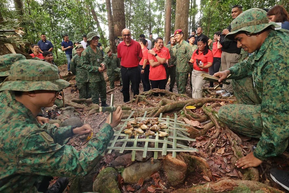 BERAMAH MESRA: Presiden Tharman Shanmugaratnam (tengah, baju merah), memerhatikan pegawai kadet Angkatan Bersenjata Singapura, yang jalani latihan di daerah Temburong, memasak ayam menggunakan api yang dihidupkan mereka. Beliau ditemani Menteri di Pejabat Perdana Menteri yang juga Menteri Kedua (Ehwal Luar merangkap Pendidikan), Dr Mohamad Maliki Osman dan Anggota Parlimen, Cik Mariam Jaafar.