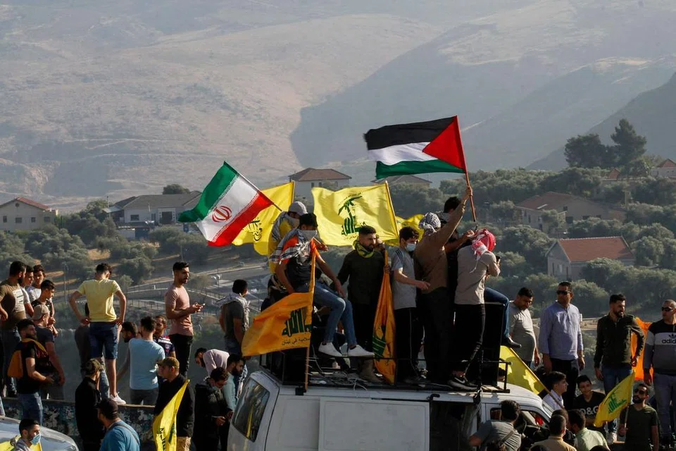 SEDIA MEMBANTU: Gambar yang dirakamkan pada 14 Mei lalu menunjukkan penyokong Hezbollah di Lebanon mengibarkan bendera mereka (kuning) dan bendera Iran (kiri) dan Palestin (kanan) semasa bantahan antiIsrael di kawasan selatan Khiam yang bersempadankan Israel, menghadap bandar Metula di utara Israel. - Foto AFP