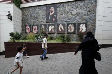 Pelawat melintasi gambar Raja Arab Saudi, Salman bin Abdulaziz Al Saud, Putera Mahkota Mohammed bin Salman, serta raja-raja terdahulu Arab Saudi ketika mereka tiba di sebuah destinasi pelancongan di Abha, Arab Saudi, pada 19 Ogos 2025.