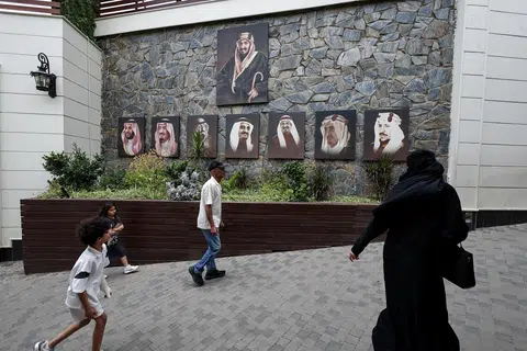 Pelawat melintasi gambar Raja Arab Saudi, Salman bin Abdulaziz Al Saud, Putera Mahkota Mohammed bin Salman, serta raja-raja terdahulu Arab Saudi ketika mereka tiba di sebuah destinasi pelancongan di Abha, Arab Saudi, pada 19 Ogos 2025.