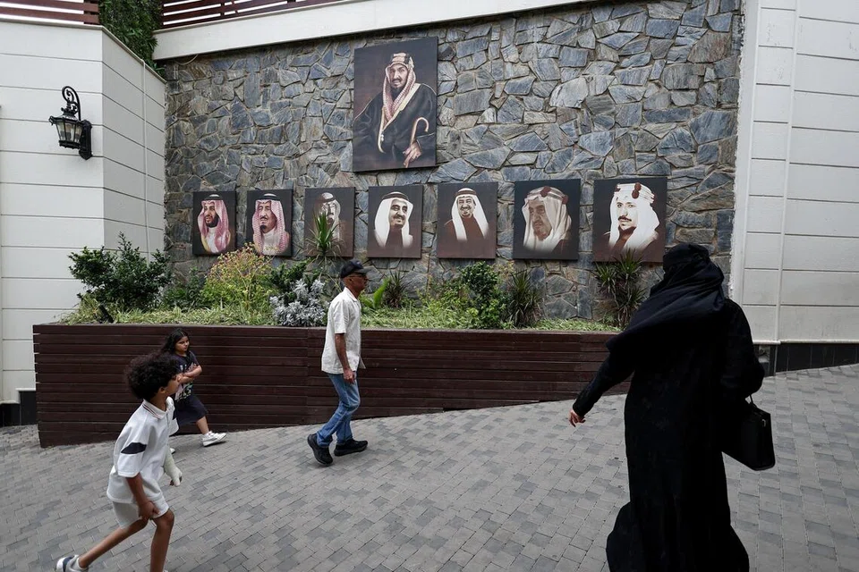 Pelawat melintasi gambar Raja Arab Saudi, Salman bin Abdulaziz Al Saud, Putera Mahkota Mohammed bin Salman, serta raja-raja terdahulu Arab Saudi ketika mereka tiba di sebuah destinasi pelancongan di Abha, Arab Saudi, pada 19 Ogos 2025.