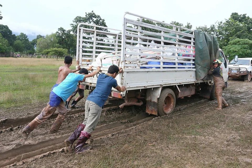 GOTONG-ROYONG: Beberapa orang tolong menolak sebuah lori yang membawa bekalan bantuan oleh Palang Merah Singapura yang terperangkap dalam lumpur sedalam enam inci dekat pusat pemindahan Sanamxay.