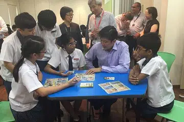 BERMAIN KAD: Encik Ng Chee Meng (duduk, berbaju ungu) mencuba permainan kad, SG Unite!, dengan pelajar darjah enam daripada Sekolah Rendah St Hilda's. - Foto THE STRAITS TIMES
