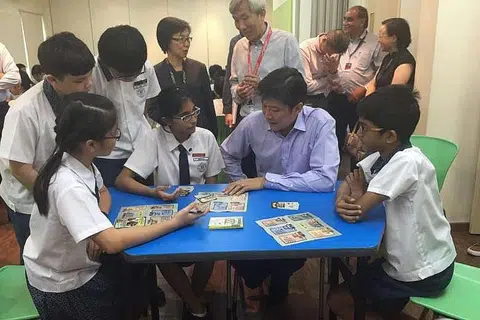 BERMAIN KAD: Encik Ng Chee Meng (duduk, berbaju ungu) mencuba permainan kad, SG Unite!, dengan pelajar darjah enam daripada Sekolah Rendah St Hilda's. - Foto THE STRAITS TIMES