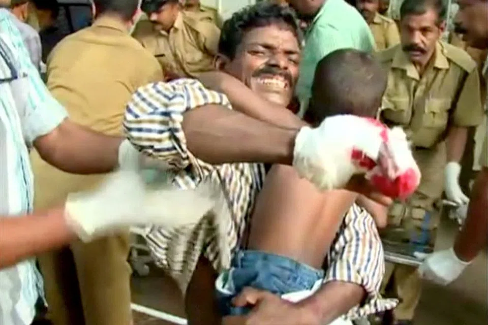 PANIK SEORANG AYAH: Seorang lelaki yang cedera memeluk erat anak beliau sebelum mendapatkan rawatan daripada pasukan perubatan di hospital menyusuli kejadian kebakaran dan letupan di Kuil Hindu Puttingal Devi, di sekitar wilayah Kollam, di Kerala, India, semalam. - Foto REUTERS