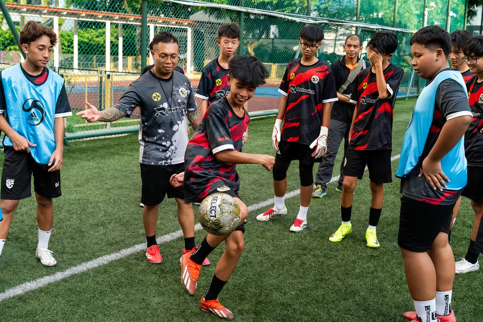 Selain mengajar teknik dan taktik bola sepak, Encik Mohammad Azimmi Jamaluddin (dua dari kiri), juga membimbing kanak-kanak dan belia yang menghadiri sesi latihan bola sepaknya sebagai sebahagian aspek kehidupan.