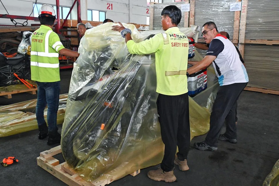 Encik Mohd Anis Mohd Kassim (kanan) membantu membalut motosikal di atas kayu palet pada 6 Disember.