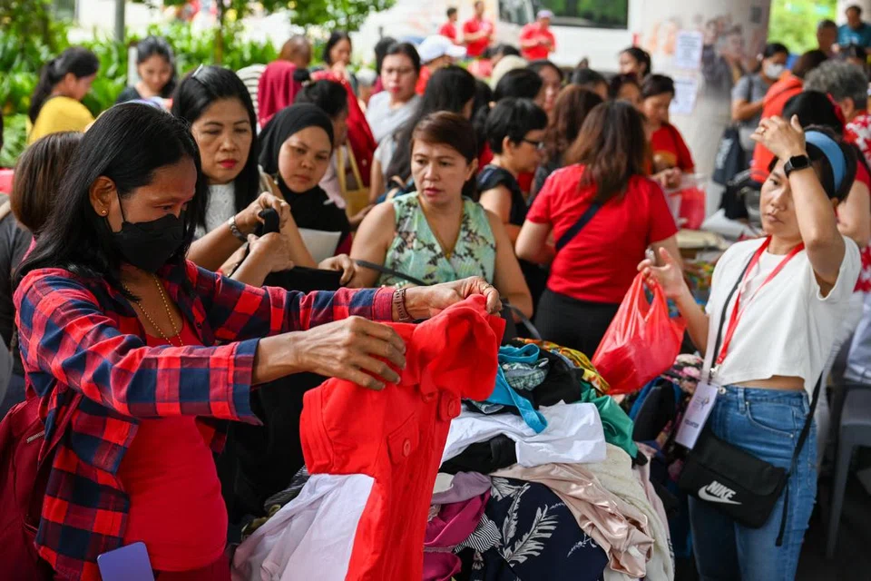 Para pembantu rumah migran (MDW) berbelanja di reruai pasar lambak yang menjual pakaian pada harga serendah $2, semasa acara Karnival Hari Kebangsaan.