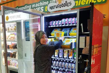 TEKNOLOGI BERI KEMUDAHAN: Cik Adilah memasukkan produk-produk makanan bayi dalam mesin layan diri yang disewanya di IMM. - Foto ihsan ADILAH LATIP