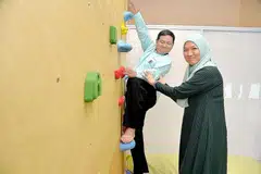 MY INSPIRING JOURNEY (MIJ) DI LOKASI BARU: Cik Faraliza Zainal membantu seorang kanak-kanak istimewa memanjat tembok di lokasi baru pusat pendidikan itu di Changi Road, yang dipertingkat hasil sumbangan sekitar $120,000 daripada orang ramai. - Foto M.O. SALLEH