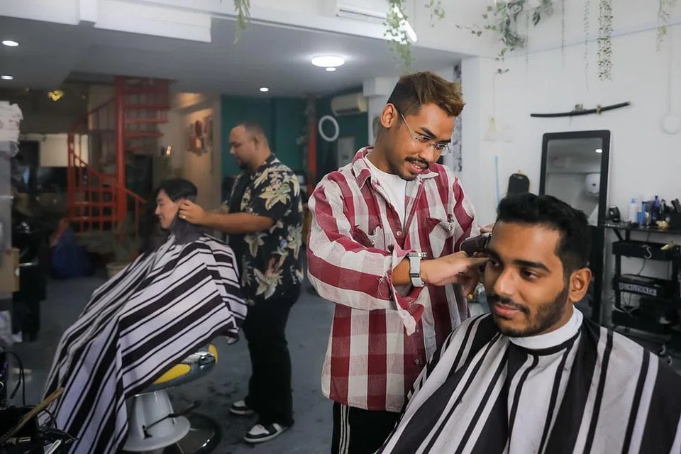 'SNIP! SNIP!': (Atas) Seorang lagi pemilik bersama Bodeiga Barbershop, Encik Taufiq Yusof, melayani pelanggan di kedainya di Boat Quay. - Foto BM oleh GAVIN FOO
