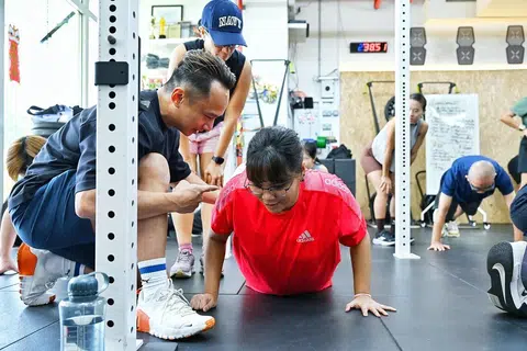 Cik Siti Fairus Rahmad (di lantai) melakukan senaman ‘push-up’ dengan nasihat daripada pengasas gim Fire City, Encik Samuel Lim (kiri), sambil disaksikan pemandu arah yang juga sukarelawan, Cik Sunita Riar (kiri, belakang).