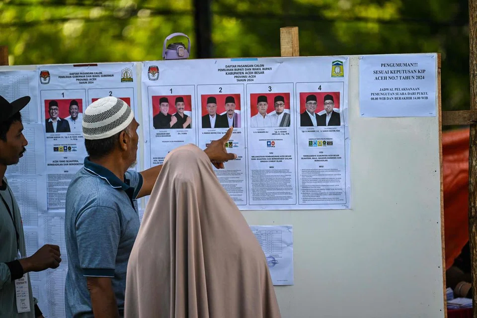Para pengundi memeriksa calon sebelum membuang undi semasa pilihan raya eksekutif tempatan bagi memilih gabenor, wali kota (datuk bandar) dan bupati (ketua daerah) di Darul Imarah, pinggir Banda Aceh pada 27 November.