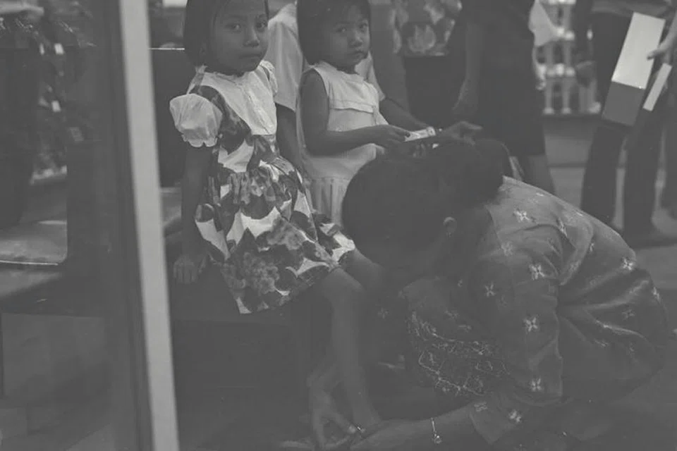 Seorang ibu menyarungkan kasut ke kaki anaknya dalam gambar yang dirakam pada 6 Janari 1967 ini. Membeli pakaian dan kasut baru antara kegiatan yang dilakukan oleh masyarakat Melayu/Islam di sini. 