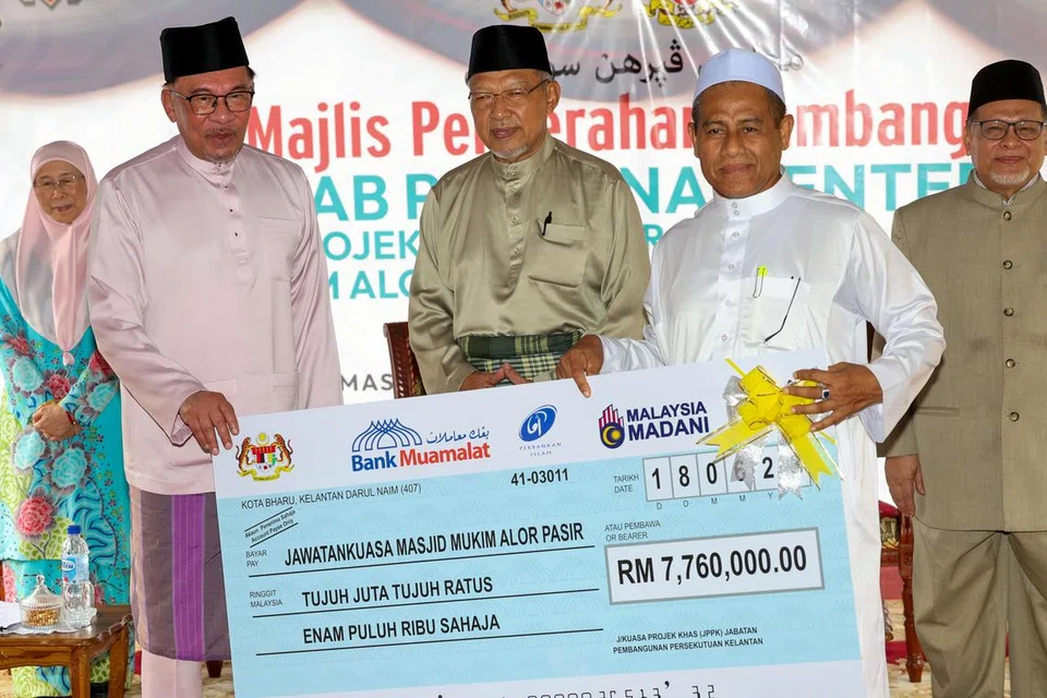 LAWATAN:  Perdana Menteri Datuk Seri Anwar Ibrahim (dua, kiri) menyampaikan replika cek berjumlah RM7.76 juta ($2.25 juta) kepada Pengerusi Masjid At-Taqwa Mukim Alor Pasir Aziz  Mohamad (dua, kanan) pada majlis penyerahan replika cek bagi projek menaiktaraf Masjid At-Taqwa Mukim Alor Pasir sempena lawatan kerja sehari beliau di Kelantan.