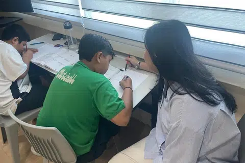 Cik Ayuni (kanan) mengajar kanak-kanak di bawah program Penglibatan Belia di Kejiranan apabila beliau ada masa lapang bersama TPCSC sejak 2023. Selain membantu dengan akademik, beliau juga membimbing kanak-kanak dalam aktivi masak dan sukan.