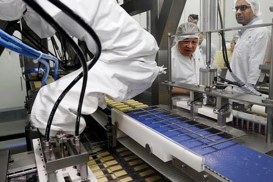 HURAIAN ROBOTIK: Encik Quah Wee Keong (kiri) sedang menerangkan kepada Encik Tharman Shanmugaratnam bagaimana 'lengan robotik' membantu menyusun dan membungkus keju, yang sebelum ini memerlukan tenaga kerja. - Foto THE STRAITS TIMES