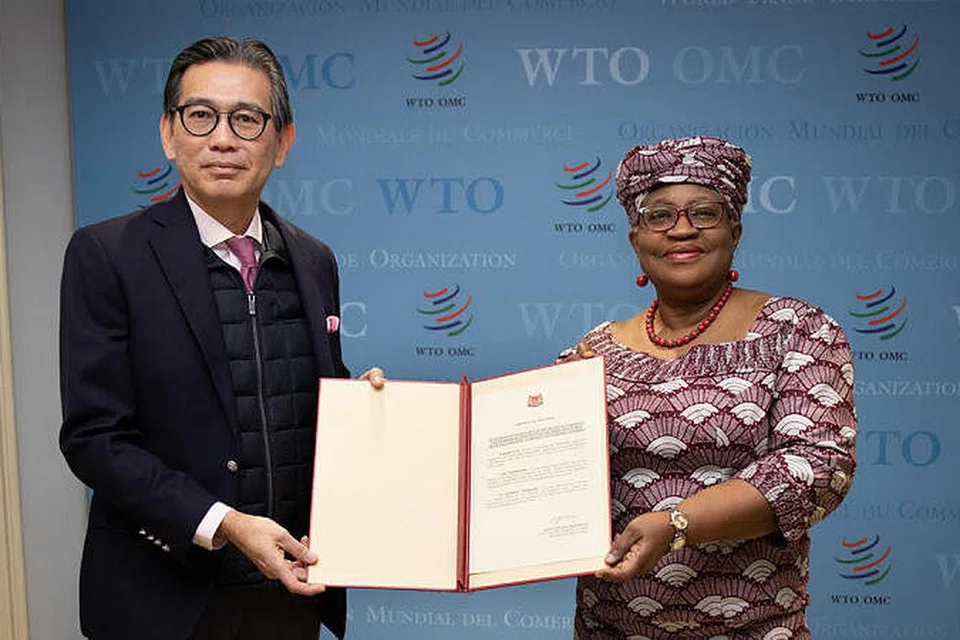 Duta Tan Hung Seng yang juga wakil tetap Singapura ke Pertubuhan Perdagangan Dunia (WTO) dan Pertubuhan Hak Cipta Intelektual Sedunia (kiri) menyerahkan penerimaan rasmi negara ini kepada Ketua Pengarah WTO, Cik Ngozi Okonjo-Iweala. - Foto WTO