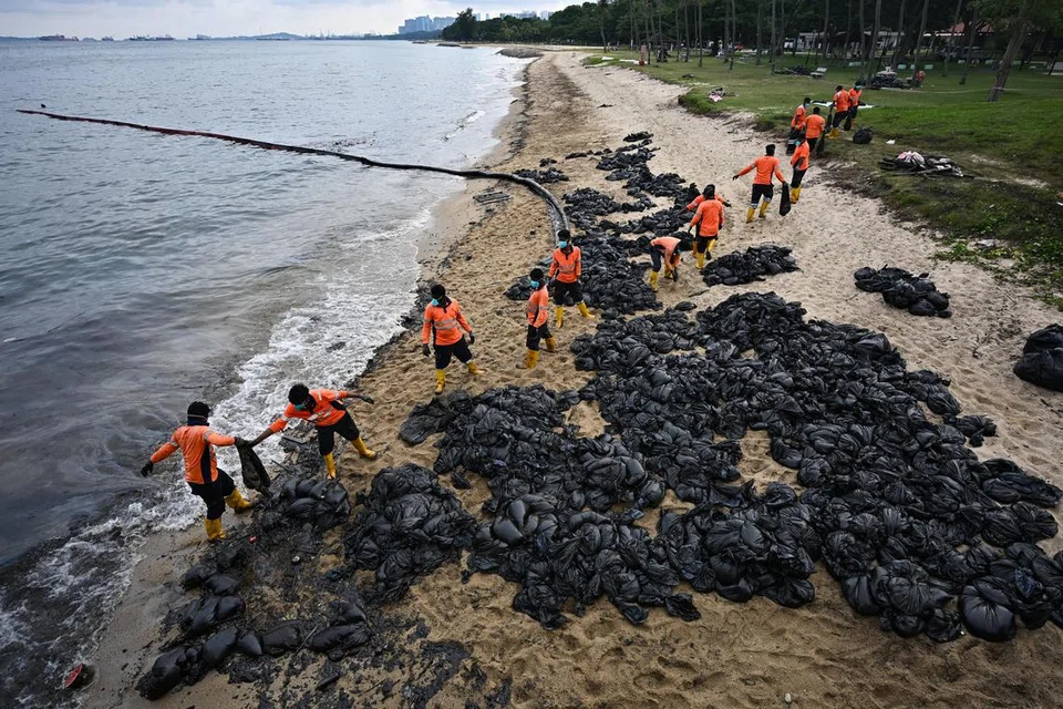 Pekerja memindahkan beg pasir berlumuran minyak untuk dilupuskan berhampiran longkang besar Siglap di Taman East Coast pada 19 Jun.