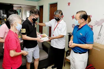KURANGKAN BEBAN: (Dari kanan) Encik Seah dan Encik William menyampaikan baucar FairPrice dan habuan sempena Tahun Baru Cina kepada Encik Ng dan keluarganya. - Foto ZAOBAO