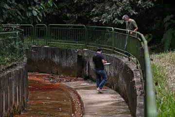 TEMPAT KEJADIAN: Salah seorang daripada dua penyiasat sedang mencatat nota setelah beliau memasuki ke dalam longkang sementara diperhatikan oleh rakan penyiasat. - Foto BH oleh KUA CHEE SIONG