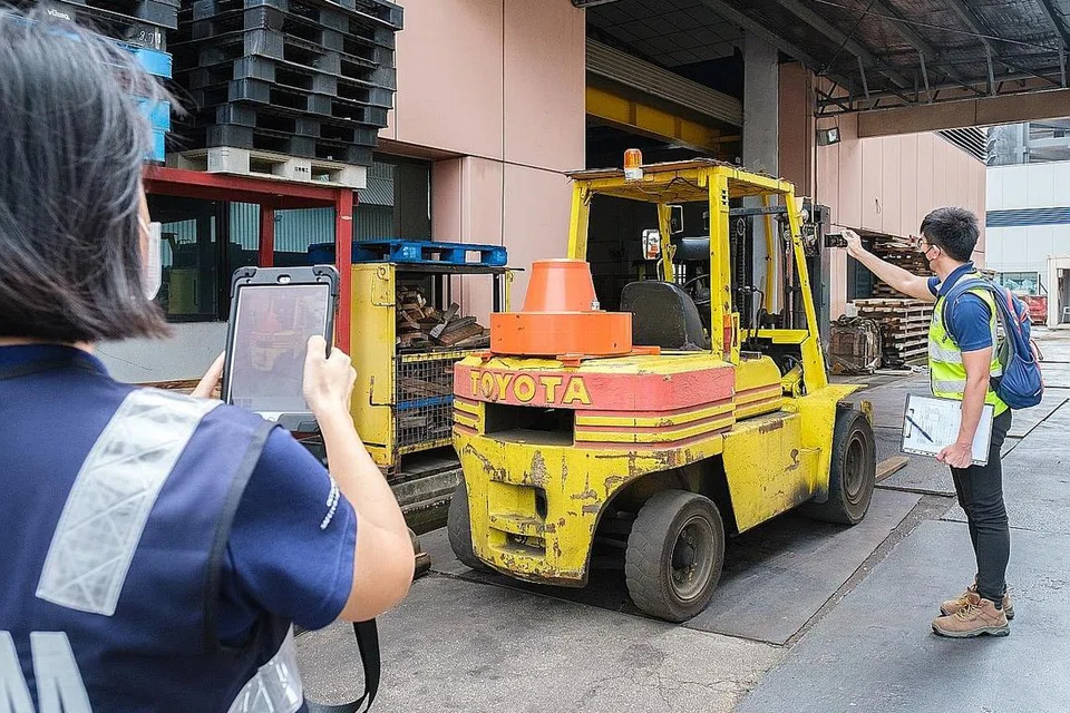 JALANKAN OPERASI PENGUATKUASAAN: Pegawai MOM melakukan pemeriksaan terhadap sebuah kenderaan forklift di sebuah tapak kerja bagi memastikan ia tidak melanggar sebarang peraturan yang boleh membahayakan pekerja. - Foto MOM