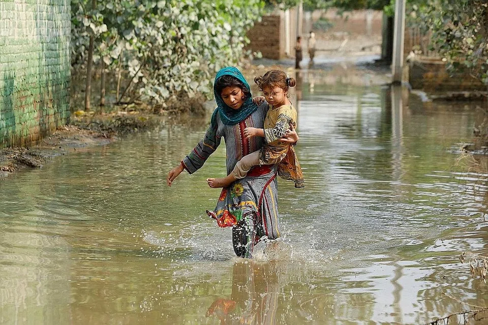MEREDAH BANJIR: Seorang kanak-kanak perempuan membawa adiknya meredah air banjir yang mencecah paras lutut, berikutan hujan dan banjir kilat semasa musim tengkujuh di bandar Nowshera, Pakistan. - Foto REUTERS