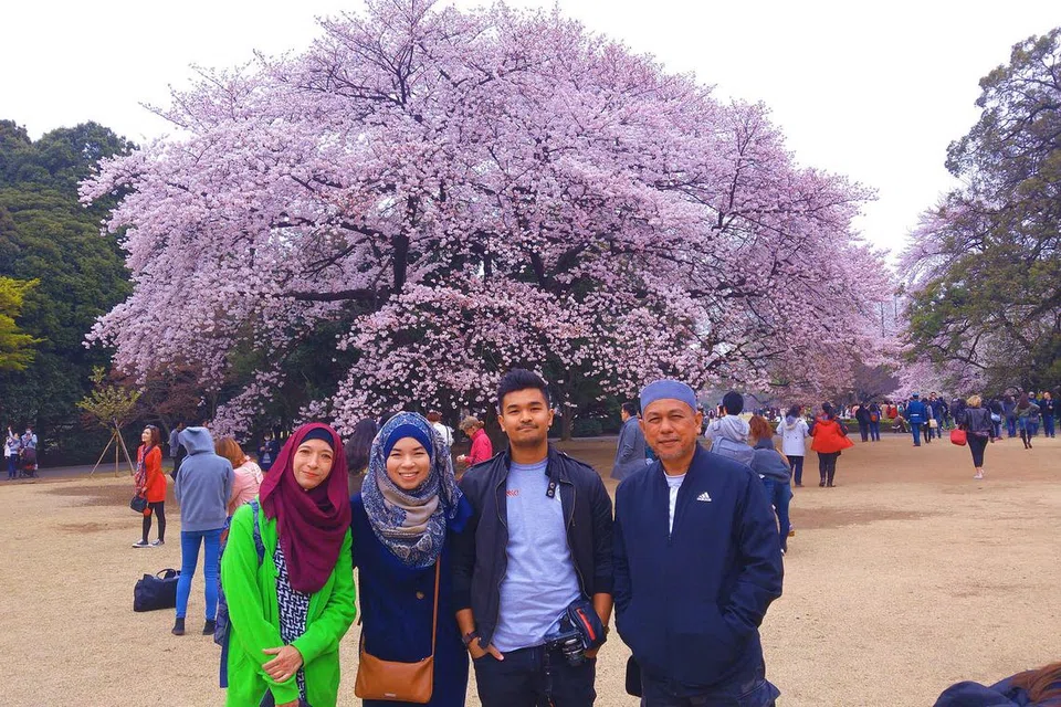 DIKELILINGI SAKURA: Penulis (bertudung biru) dan keluarga (dari kiri) ibu Cik Noorhayati Hassan, adik Encik Muhammad Nordin dan ayah Encik Nordin Ibrahim, di Taman Shinjuku, Tokyo. - Foto-foto SITI AISYAH NORDIN