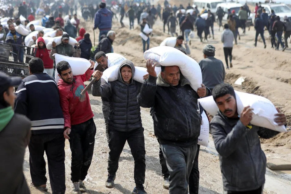 Rakyat Palestin membawa beg berisi tepung yang diagihkan daripada trak bantuan berhampiran pusat pemeriksaan Israel di tengah-tengah konflik berterusan antara Israel dan Hamas.