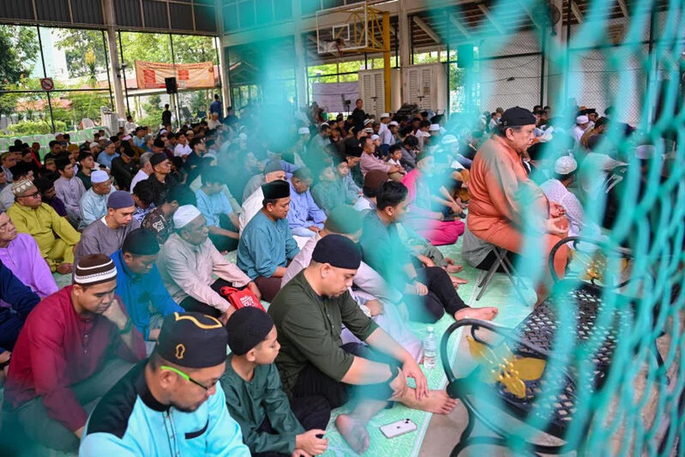 BUAT PENYESUAIAN: Penduduk Yishun menunaikan solat Aidiladha di gelanggang keras dekat Blok 327 Yishun Ring Road pada pagi Khamis, iaitu salah satu tempat solat yang disediakan Masjid Darul Makmur.
