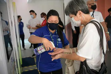 SANITISER PERCUMA: Pembantu mesin layan diri, Cik Tang Li Ring, 44 tahun, membantu seorang penduduk mencuba sanitiser percuma di Pusat Masyarakat Yew Tee semalam. - Foto BH oleh NG SOR LUAN