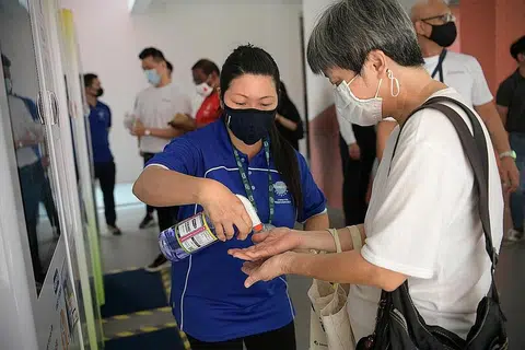 SANITISER PERCUMA: Pembantu mesin layan diri, Cik Tang Li Ring, 44 tahun, membantu seorang penduduk mencuba sanitiser percuma di Pusat Masyarakat Yew Tee semalam. - Foto BH oleh NG SOR LUAN