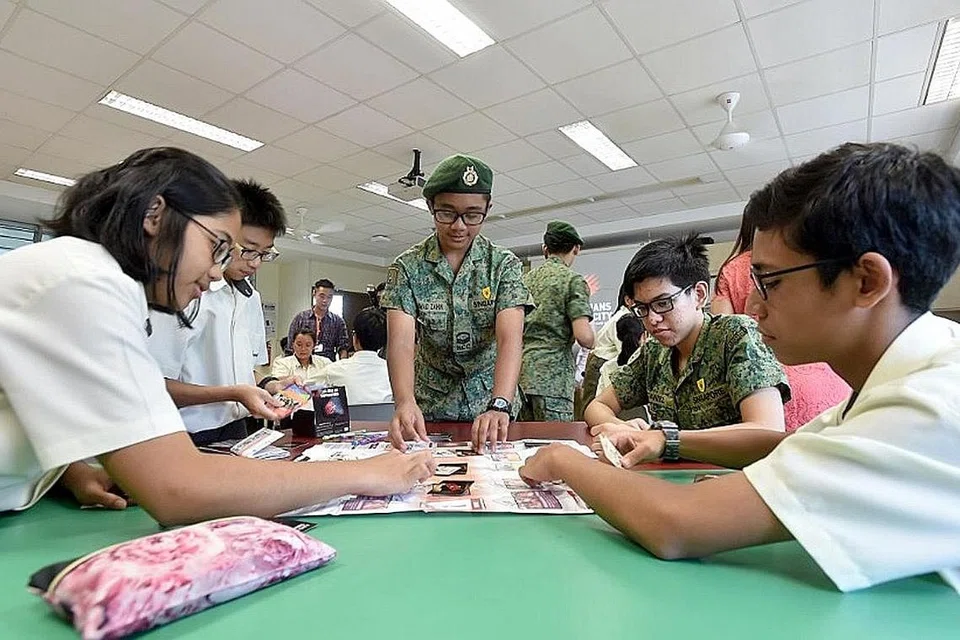 BELAJAR SAMBIL BERMAIN: Para pelajar daripada kumpulan beruniform Sekolah Menengah Greendale sedang mengajar teman-teman mereka di menengah dua cara bermain permainan kad 'Guardians of the City' (GOTC). - Foto-foto MINDEF 