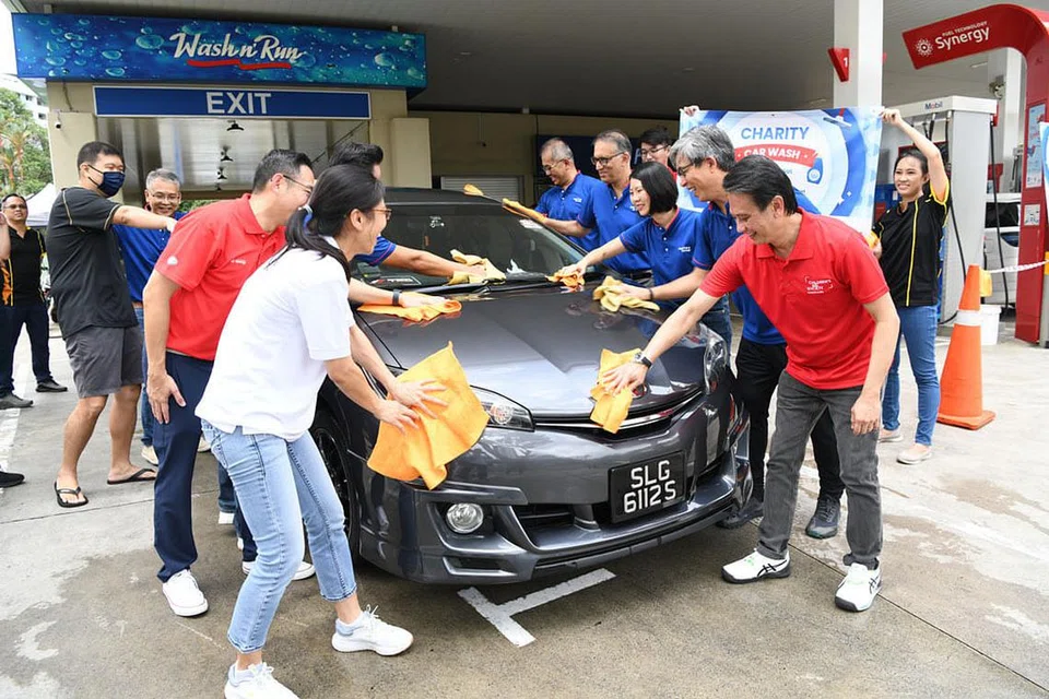 CUCI DEMI AMAL: Encik Vipul Chawla (empat dari kanan) bersama pasukan dari FairPrice, Cheers, ExxonMobil dan Persatuan Bantuan Kanak-kanak serta relawan membantu mencuci kereta. - Foto FAIRPRICE