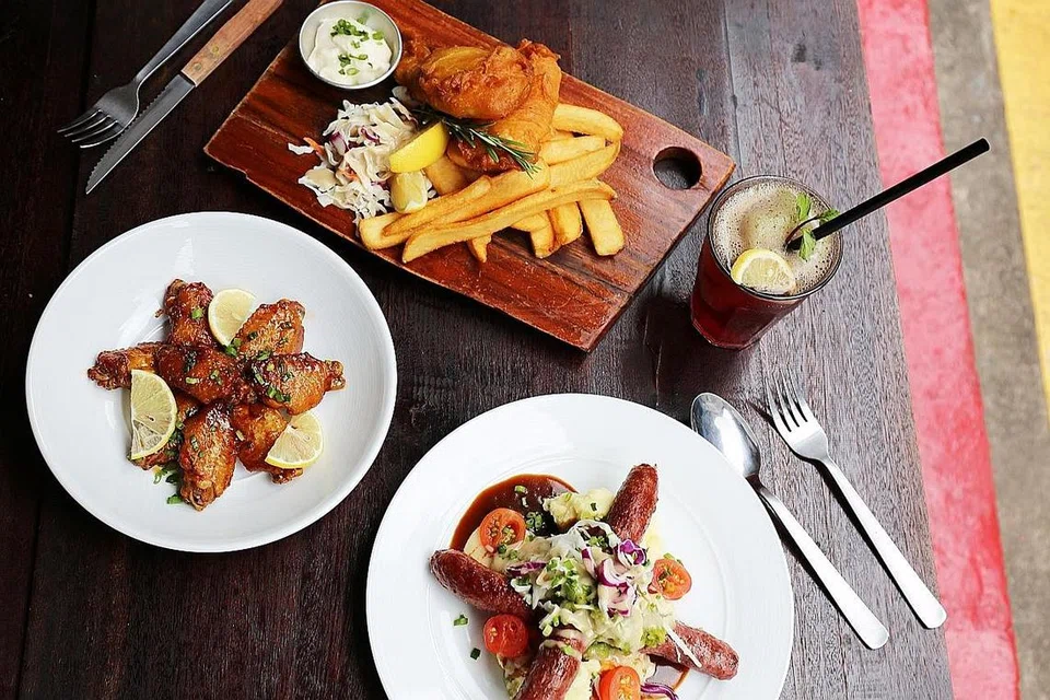 SEDAP DAN MENYELERAKAN: Kafe The Mad Sailors menyajikan hidangan menyelerakan seperti (dari kiri, ikut putaran jam) snek kepak ayam madu marmite yang dinamakan Marmite Honey Wings, hidangan 'fish and chips' dengan ikan haddock, minuman Berry Bena dan sajian 'bangers and mash'. - Foto NUR AMANINA ISMAIL