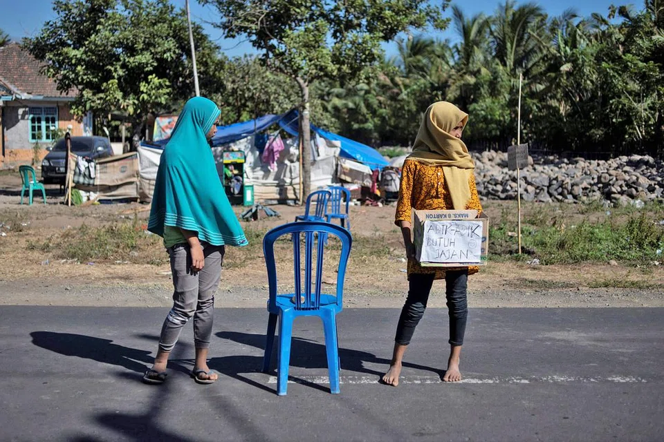 MOHON BANTUAN: Dua penduduk kampung Sambelia yang merupakan mangsa gempa menantikan kenderaan yang berlalu di situ bagi mendapatkan derma. - Foto AFP