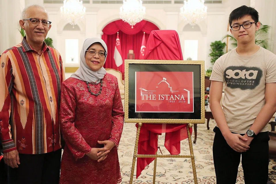 ULANG TAHUN KE-150: Presiden Halimah Yacob, yang bersama suami, Encik Mohamed Abdullah Alhabshee, melancarkan logo 'Istana 150' semasa rumah terbuka Istana sempena Deepavali semalam. Bersama mereka ialah pereka logo itu, Encik Charlie Chua, seorang pelajar dari Sota. - Foto BH oleh JONATHAN CHOO